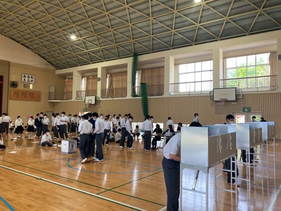 体育館に設置された投票所で並んで、投票する生徒たちの写真