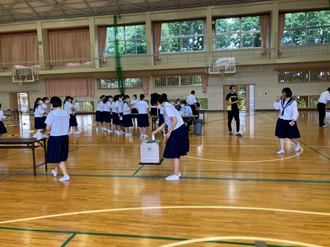 体育館に設置された投票所で並んで投票する生徒たちの写真