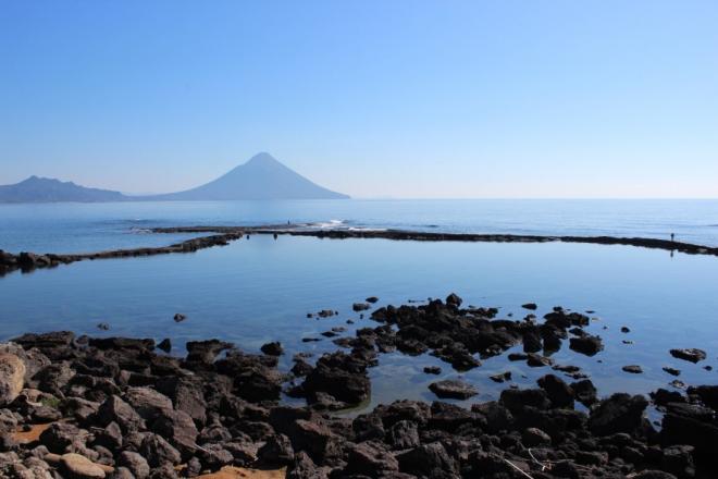 海の向こうに開聞岳を眺める番所鼻自然公園にて、干潮の時間に現れる環状型の岩礁の写真