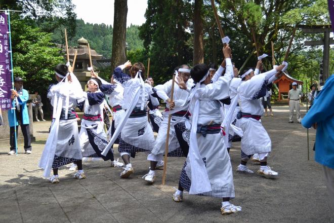 飯倉神社境内の参道にて、見学客が見守る中、揃いの白い衣装に身を包んだ白いハチマキ姿の男性陣が3列縦隊で六尺棒と三尺棒を使い舞を披露している松崎棒踊りの写真