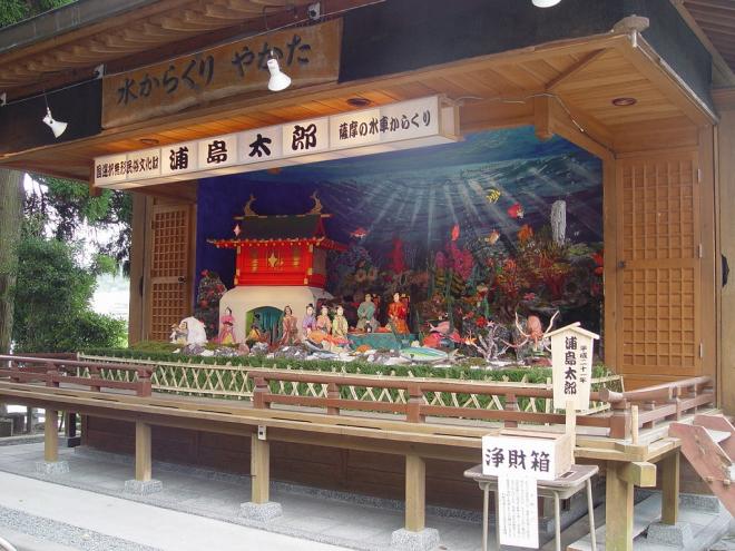 水からくりやかたの木看板が設置された屋根付きの舞台上に、国選択無形民俗文化財 浦島太郎 薩摩の水車からくりと記載された白い横長灯籠の下、浦島太郎や海の中の竜宮城、乙姫やたくさんの魚たちのからくり人形の写真