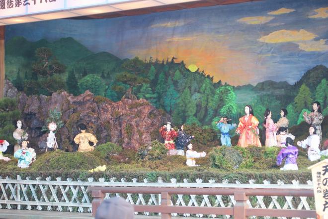 舞台上で、天の岩戸に閉じこもってしまった太陽の神アマテラスを岩戸から引き出そうとしている神々のからくり人形の写真