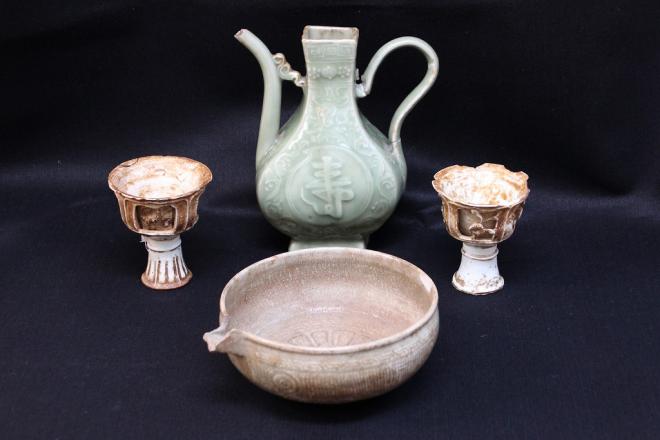 黒い背景に、左右対称に配置された青磁器で作られた馬上杯、中央手前は丸い器の高麗系青磁で作られた片口、中央奥には青磁で作られた青い福寿の花瓶が並べられた写真