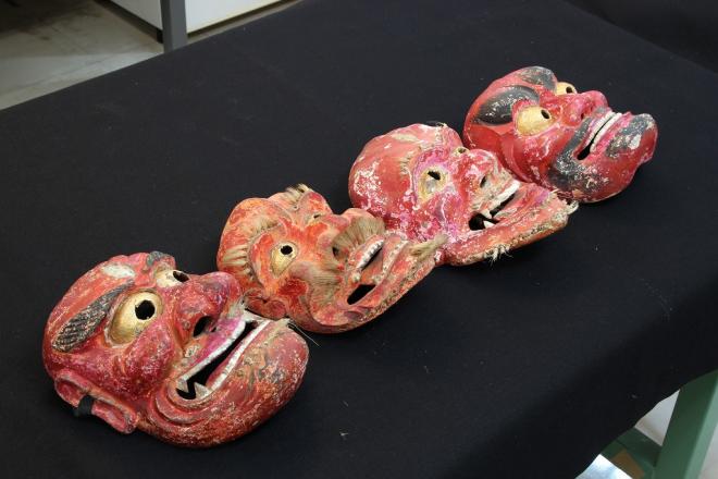 黒い台座に、横一列に4つ並べられた大きな目・鼻・口をした赤色の神舞面の写真