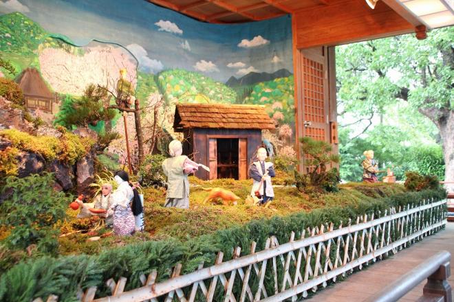 のどかな里山風景が設置された舞台上で、中央の犬が「ここ掘れワンワン」と吠えた場所をおじいさんとおばあさんが掘り起こそうとしている、からくり人形の写真