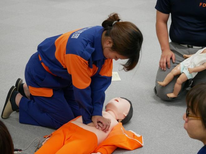 女性消防団員が訓練用の人体モデルを使って、ヒジを伸ばし手を重ねて人体モデルの胸に置いて胸骨圧迫をしている様子の写真