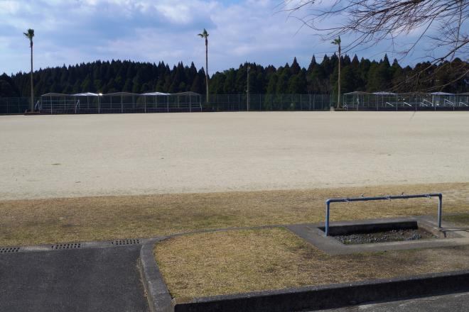 後方には林が立っており、フェンスで囲まれ場所に広々としたグラウンドがあり、手前には芝生のスペースがある南九州市知覧平和公園サッカー場の写真