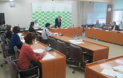 コの字に長机が配置された会議室内で、南九州市のバックパネルの前に置かれた長机の前に市長が立ち話をしている様子の写真