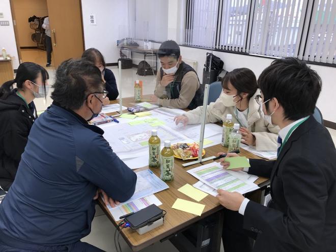 グループでの話合いで、出てきた意見が書かれた付箋が模造紙に沢山貼られており、女性が付箋を指し話会いが行われている様子の写真