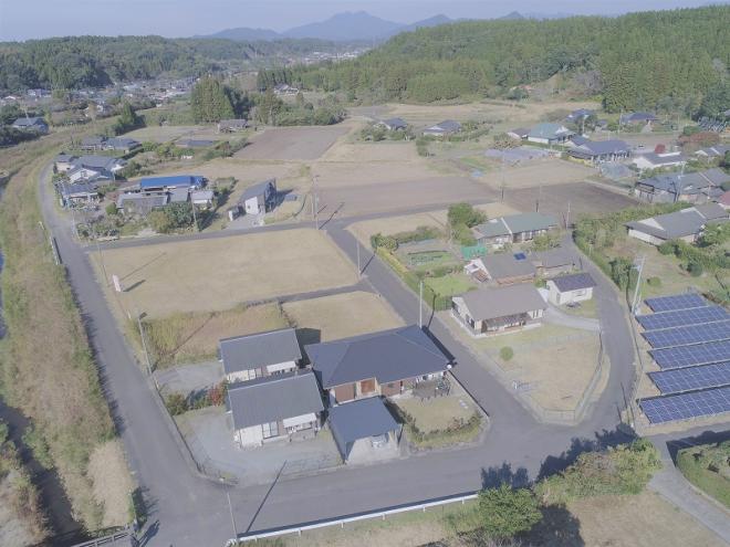 奥に山脈が広がり、緑・グレーの屋根の家が建ち並んでいる団地を上空から撮影した写真