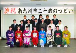 「祝南九州市二十歳のつどい」と書かれた横断幕が掲げられ会場の壁の前で、色とりどりの振袖を着た女性と、袴やスーツを着た男性の新成人が3列に並んで写した記念写真