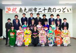 「祝南九州市二十歳のつどい」と書かれた横断幕が掲げられ会場の壁の前で、色とりどりの振袖を着た女性と、スーツを着た男性の新成人が3列に並んで写した記念写真