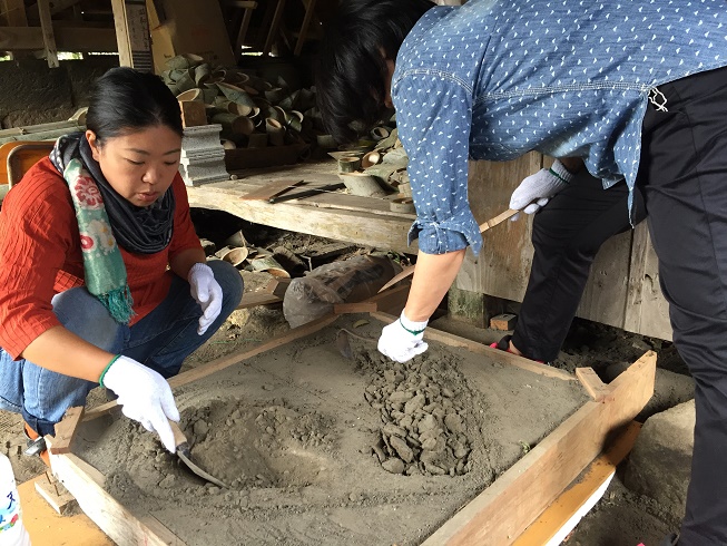 木枠の中に砂を入れしゃがんでスコップを使い作業している南九州市地域おこし協力隊・岩崎泰依さんと、一緒に作業している方の写真
