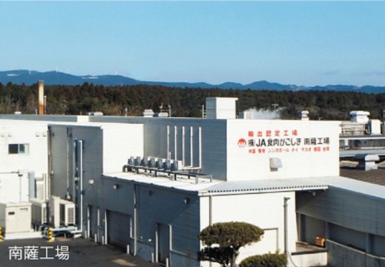 奥に山脈が広がり、白を基調とした2階建ての建物から湯気が上がっている株式会社JA食肉かごしま南薩工場の写真