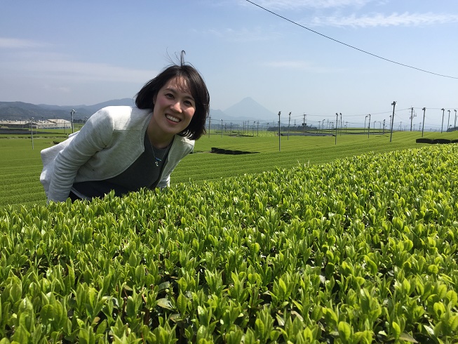 一面に広がった茶畑で、体をお茶の葉に近づけて笑っている南九州市地域おこし協力隊・川口塔子さんの写真