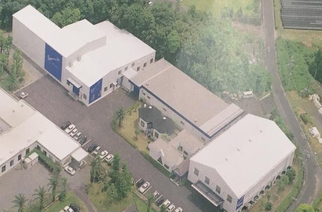 白を基調とした建物が3棟あり、敷地の中央に駐車場がある株式会社ライフドリンクカンパニーを上空から撮影した写真