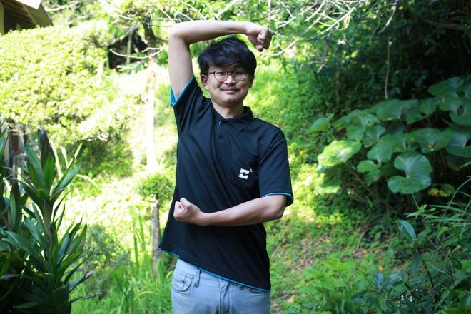 草木を背景に、拳を握ってポーズを取っている南九州市地域おこし協力隊・前迫昇吾さんの写真