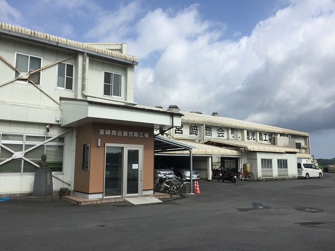 白を基調とした2階建ての建物で入口の左側に銅像が建てられている株式会社宮崎商会 鹿児島工場の写真