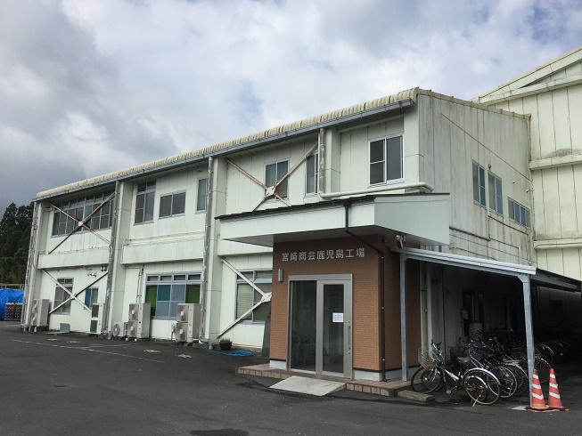 白を基調とした2階建ての建物で入口の右側に自転車が停まっている株式会社宮崎商会 鹿児島工場の写真
