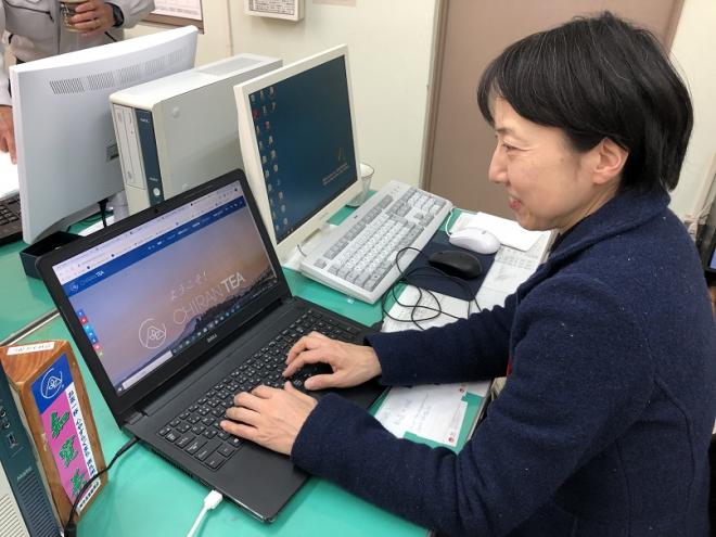 自席に座り、黒いパソコンを使って作業としている南九州市地域おこし協力隊・高久博子さんの写真