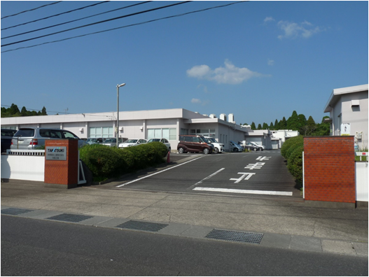 社名の看板ある門の奥に白を基調とした1階建てと、2階建ての建物がある高槻電器工業株式会社 知覧工場の写真