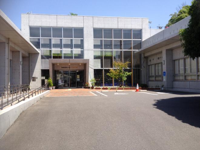 コンクリート調の建物で、コの字型に建物が隣接しており、玄関前に優先駐車場が2つある市民交流センターひまわり館の外観写真