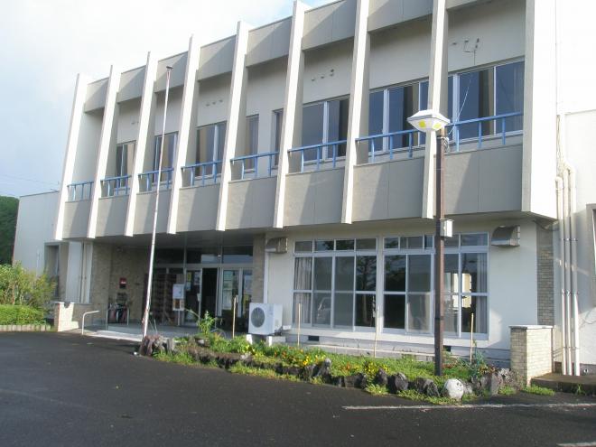 入り口右手前の花壇の中に外灯が設置され、白壁で2階建ての上別府地区公民館の外観の写真
