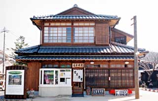 窓に木の格子がついた窓枠がついている、木造2階建ての瓦屋根の建物で、入り口の上には「富屋食堂」と書かれた木の看板と、白い暖簾がかかっている富屋食堂の外観写真