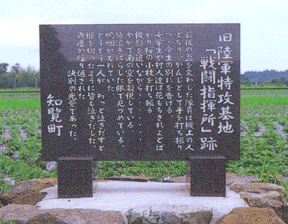 緑の畑の手前に設置された石の台座にたてられた、四角く光沢のある濃いグレーの石に「旧陸軍特攻基地戦闘指揮所跡」と白い文字で刻まれ、続けて当時の様子が書かれた石碑の写真