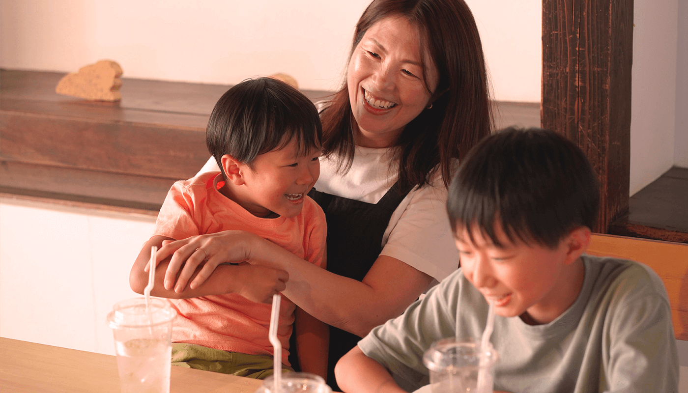 お母さんとその膝の上に載る小さな男の子、お母さんの隣に座る小学生くらいの男の子が笑顔で微笑んでいる様子の写真