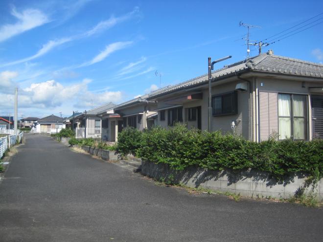 道路に沿って道路右側の高さの低いブロック塀の奥に数件の住宅が建っている市営住宅 公営青戸上団地の写真
