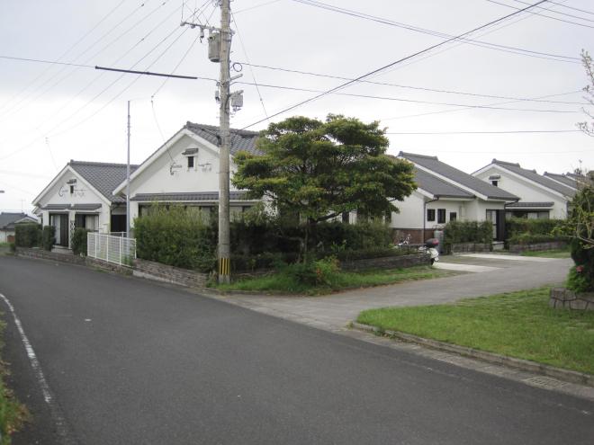 三角屋根、白い外壁の1階建て住宅が数件並んでいる市営住宅 公営・特公賃ウッドタウンえい団地を道路側から写した写真