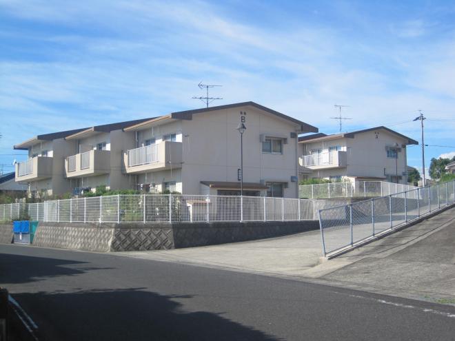 三角屋根2階建ての団地が、道路側と奥に2棟建っている市営住宅 公営椿山団地の写真