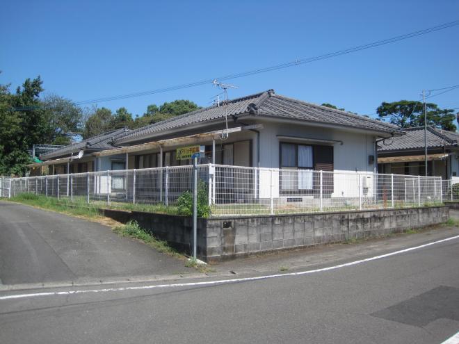 白いフェンスで囲まれ道路より少し高い場所に建っている瓦屋根の1階建て住宅が数件並んでいる市営住宅 特公賃大久保団地の写真