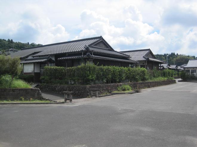 石造りの塀の上に垣根があり、垣根の奥に瓦屋根平屋建て住宅が2軒並んでいる市営住宅 公営ウッドタウン知覧団地の写真