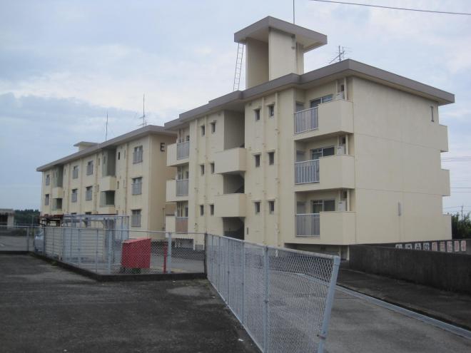 金網のフェンスの奥に3階建てのE棟とI棟が横並びに並んで建っている市営住宅 公営知覧松山団地E・I棟の写真