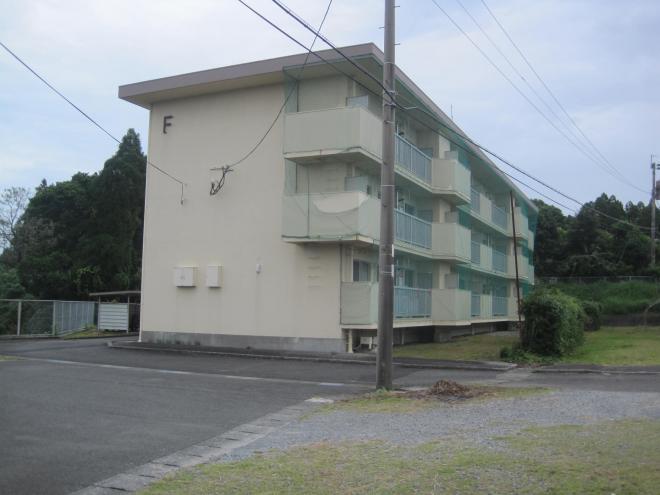 薄いクリーム色の外壁で建物側面左上に「F」とあり、ベランダ側に鳥除けネットがされている3階建ての市営住宅 公営松ヶ浦団地F棟の写真