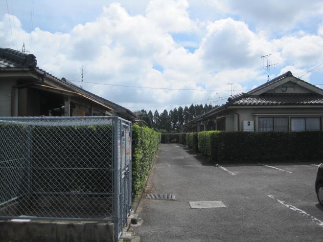 右手前に駐車場、垣根で囲まれた複数の一軒家の住宅が中央の通路の両側に並んで建っている市営住宅 特公賃徳原団地の写真