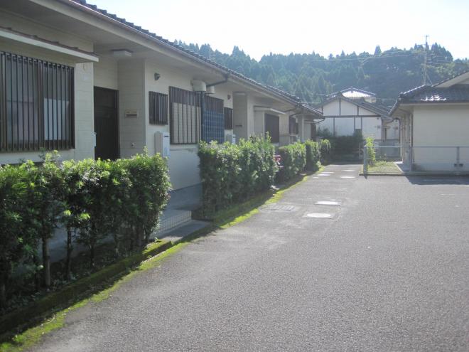 建物正面に垣根があり、瓦屋根1階建てで奥に長い建物の市営住宅 特公賃大堀迫団地の写真