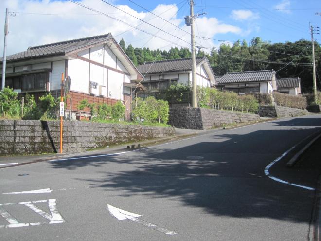 緩やかな上り坂に沿って左側に三角屋根平屋建ての住宅が4軒並んでいる市営住宅 一般ウッドタウン知覧団地の写真