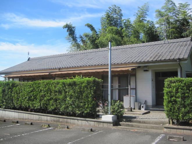 手前から駐車場、垣根とあり、奥に瓦屋根平屋建ての住宅が建っている市営住宅 一般浮辺団地の写真