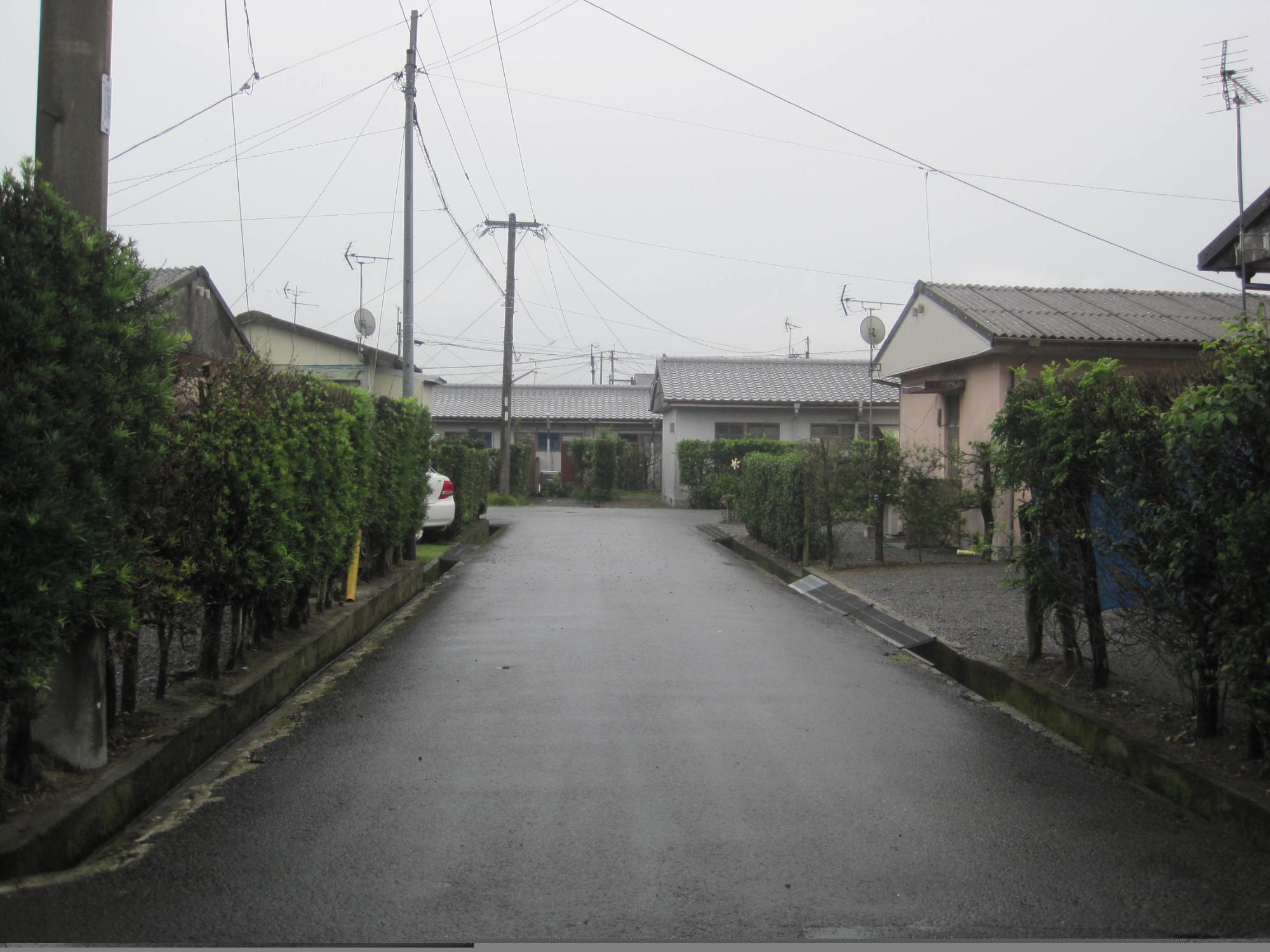 垣根の奥に三角屋根平屋建ての住宅が中央にある道路の両側と正面に建っている市営住宅 公営稲荷町団地の写真