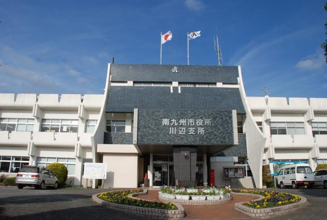 円形の花壇アーチの奥に白を基調とした2階建て南九州市役所川辺支所の写真