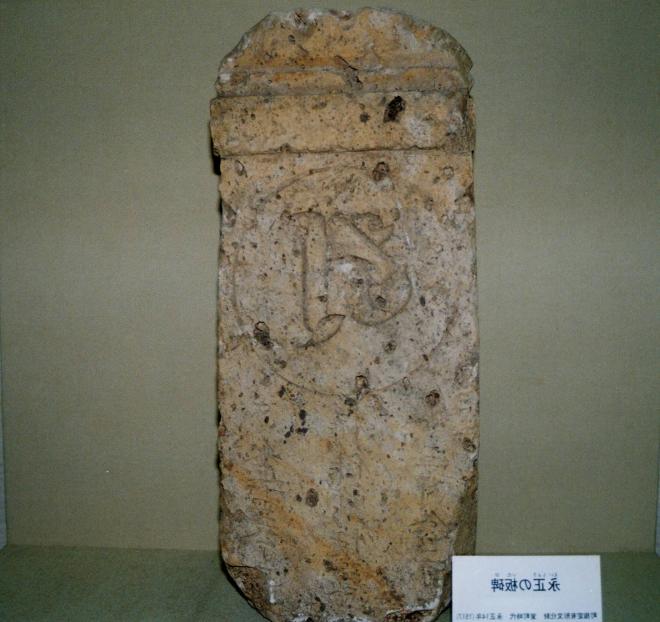 所々かけたり削れたりしているスケートボードのような形の板に文字が刻まれている永正の板碑の写真
