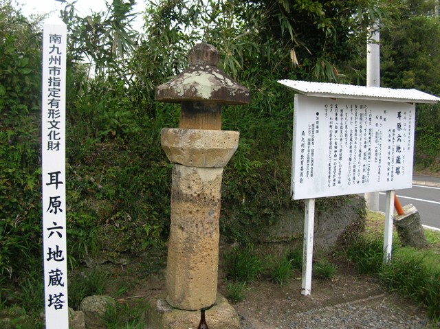 下から基礎・塔柱・中台・龕部、笠、宝珠の部分で構成され、中台と笠が十二角形の特徴を持っている、標柱と説明板の間に立つ耳原六地蔵塔の写真