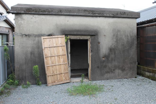 コンクリートで作られた建物に、中央には出入り口用の木製扉のみが設置された旧知覧飛行場油脂庫の外観写真