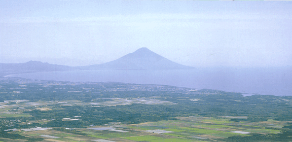 遠くに開聞岳が霞んで見え、手前に田畑や民家が点在している知覧町付近を高台から撮影した写真