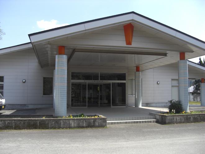 平屋建てで三角屋根の建物であり、正面入り口前には雨除け付きの降車スペースが設けられている南九州市川辺農業構造改善センターの写真