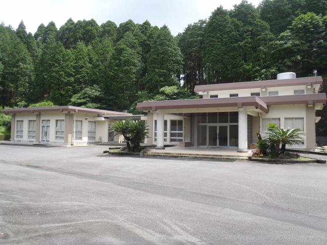 木々に囲まれ、ピンクの屋根にクリーム色の外壁の川辺火葬場の写真
