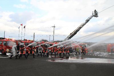 大勢の消防団員が横一列に並び，一斉に放水をする画像
